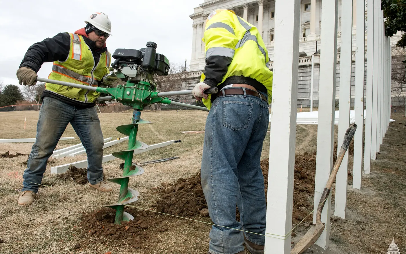 Fence crew digging post holes with a gas auger next to a new steel fence line