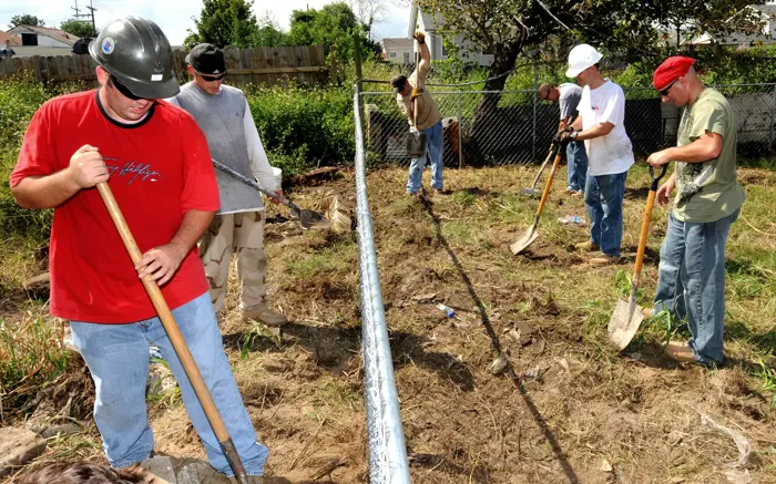 Crew digging post holes by hand near a fence line